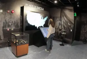 Honoring History: Exhibit Studios' Remarkable Civil War Battle Flag Exhibit Exhibit Studios small bog shaped display with glass cube over tope to protect artifacts on left. Girl using touch screen center.