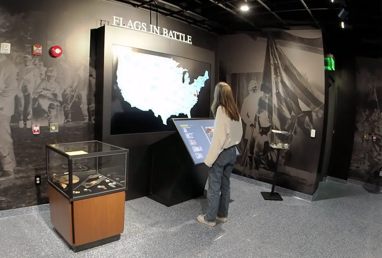 Honoring History: Exhibit Studios' Remarkable Civil War Battle Flag Exhibit Exhibit Studios small bog shaped display with glass cube over tope to protect artifacts on left. Girl using touch screen center.