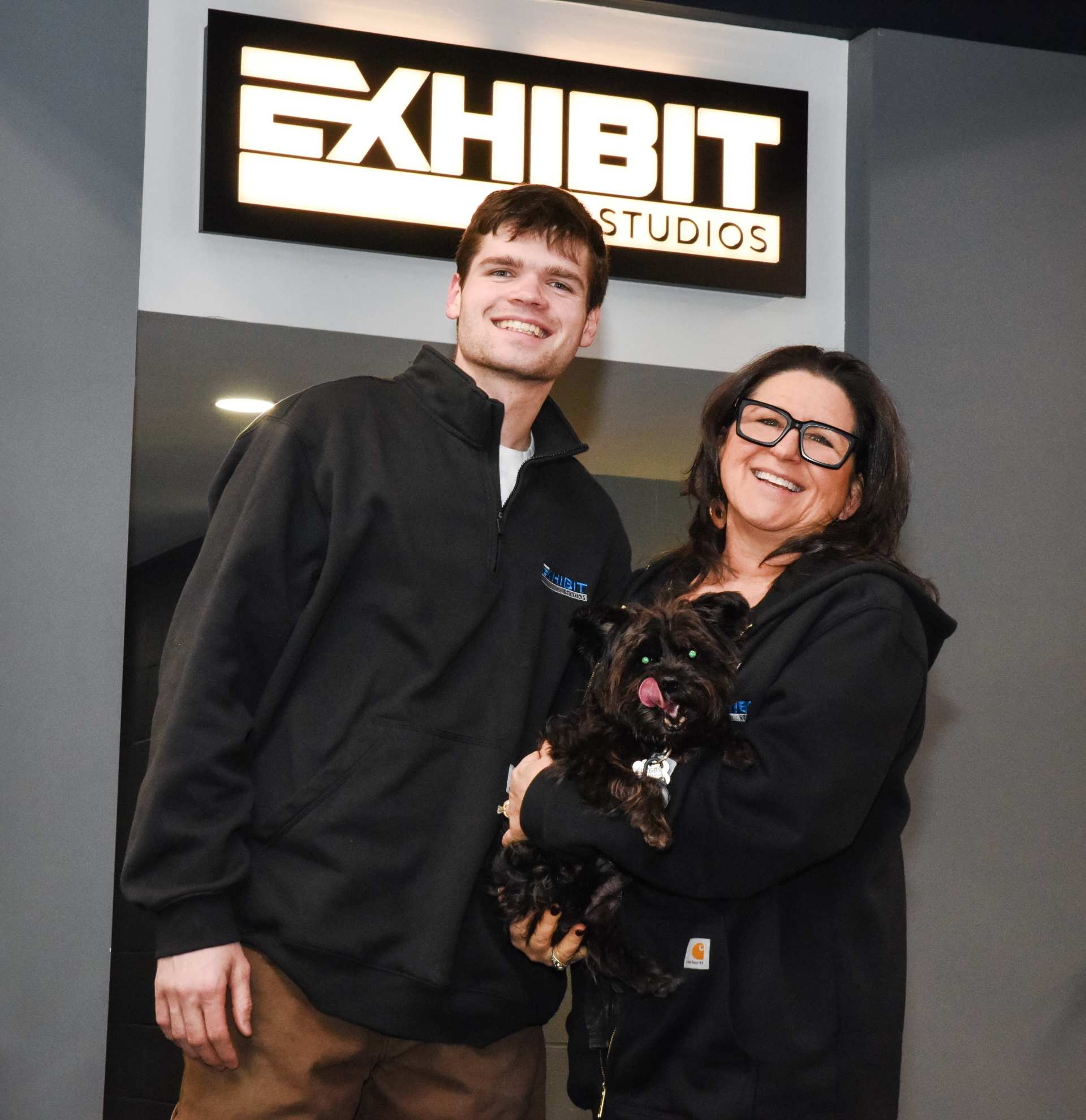 2 Exhibit Studios employees standing by the Exhibit Studios sign