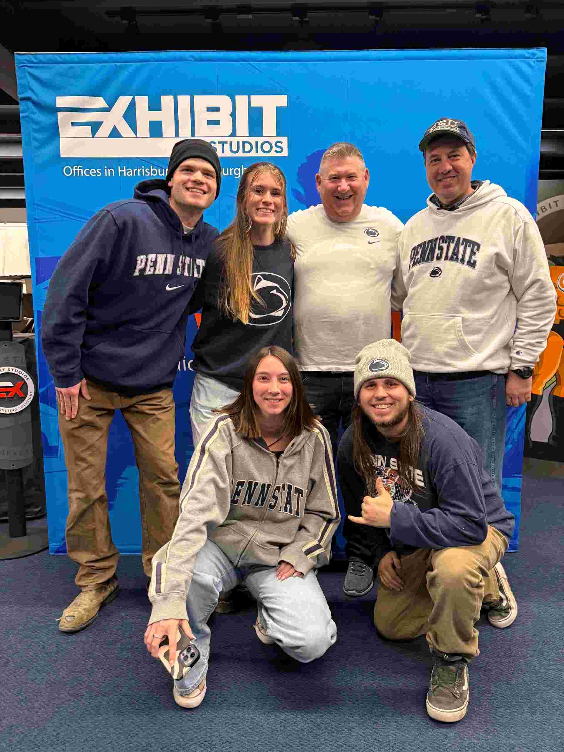 Exhibit Studios employees taking a group photo by their logo